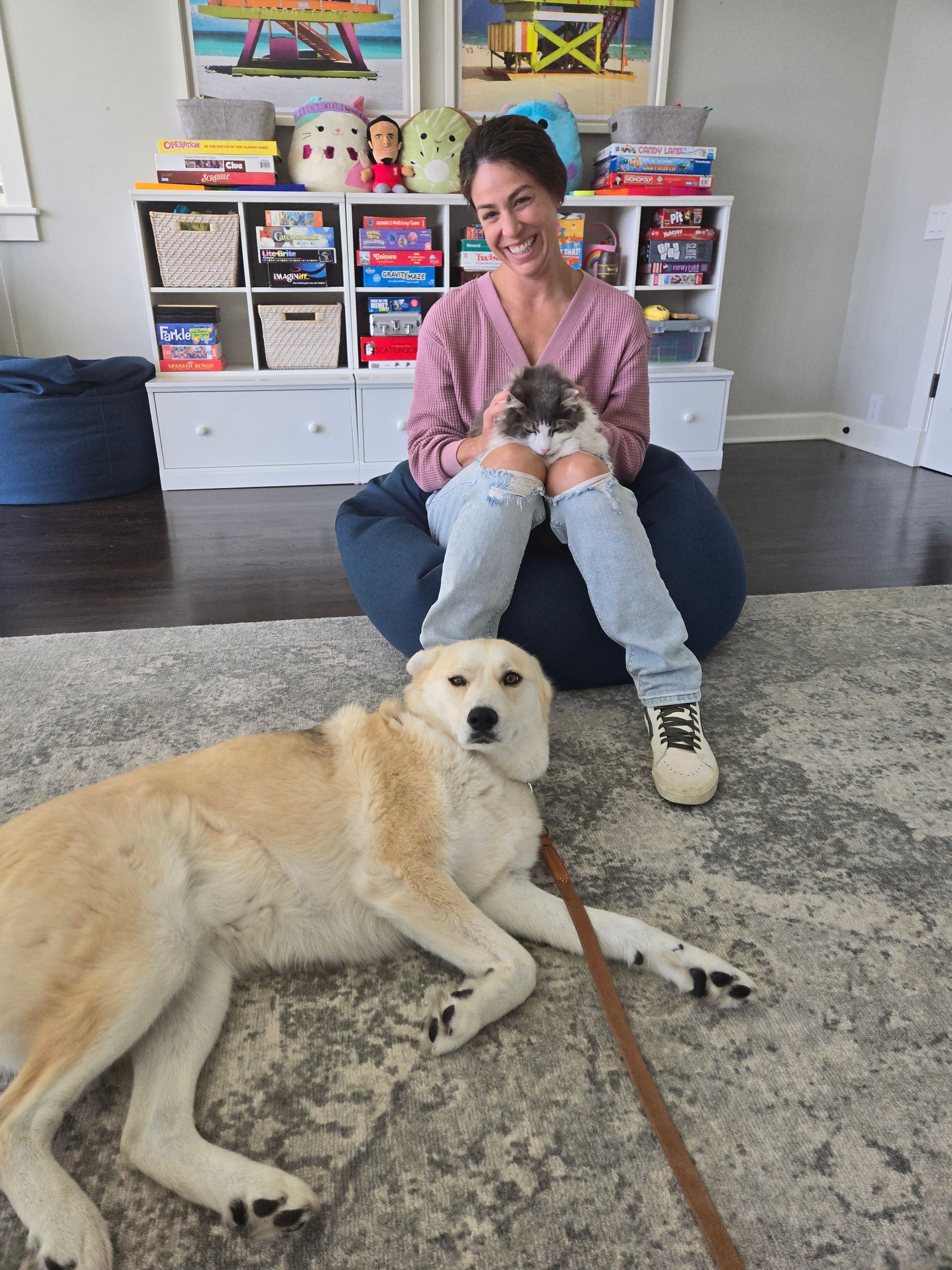 A woman is sitting on a bean bag chair next to a dog laying on the floor.