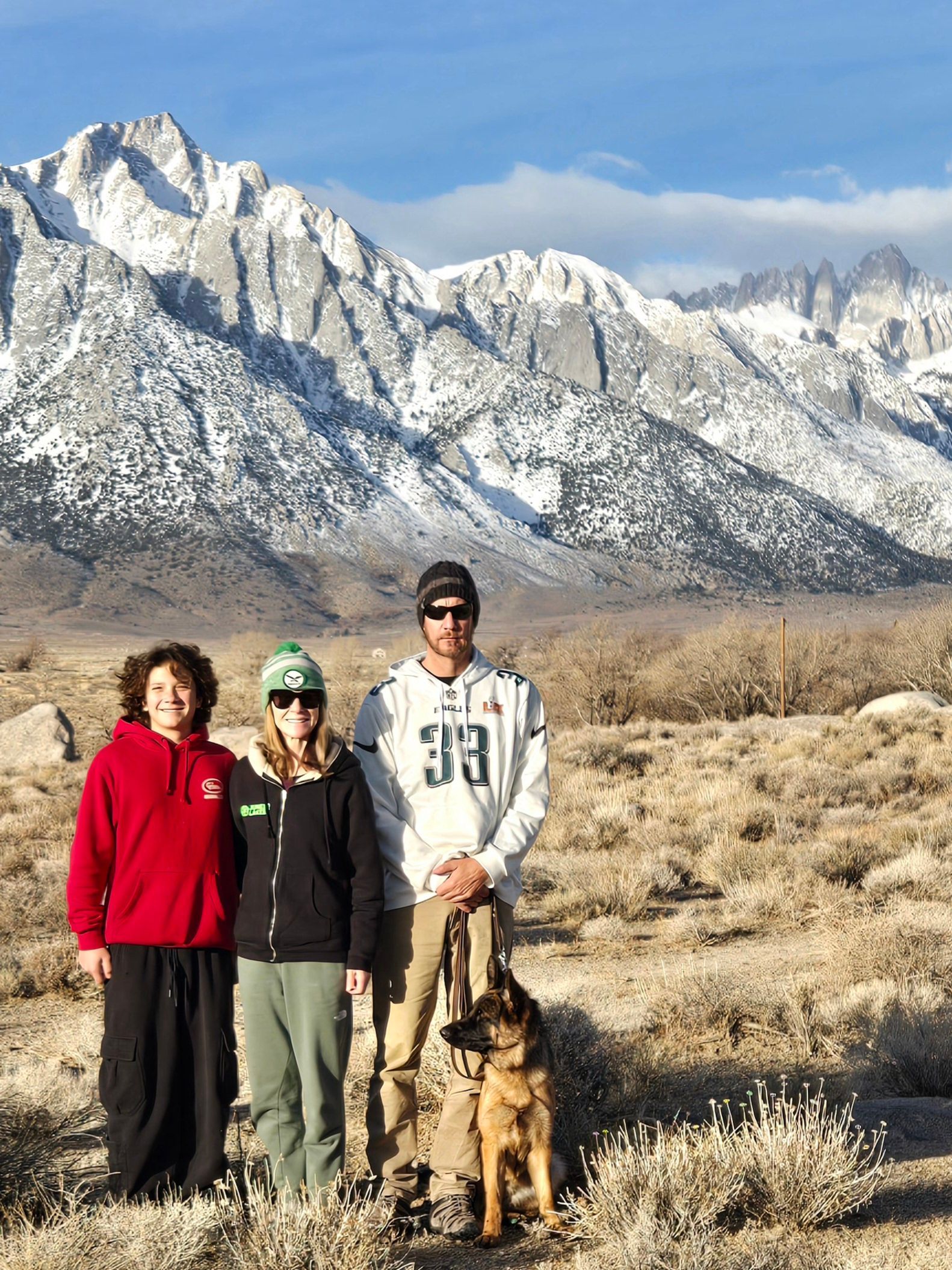 A group of people and a dog are standing in front of a snowy mountain.