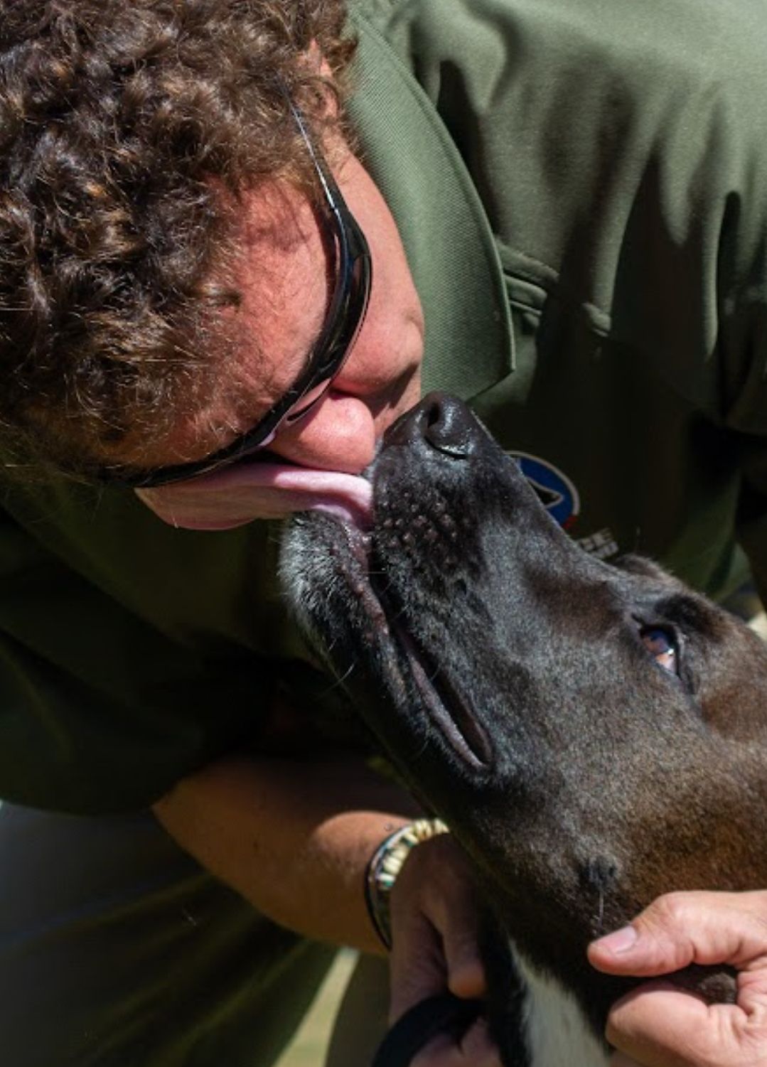 A man is kissing a black dog on the nose.