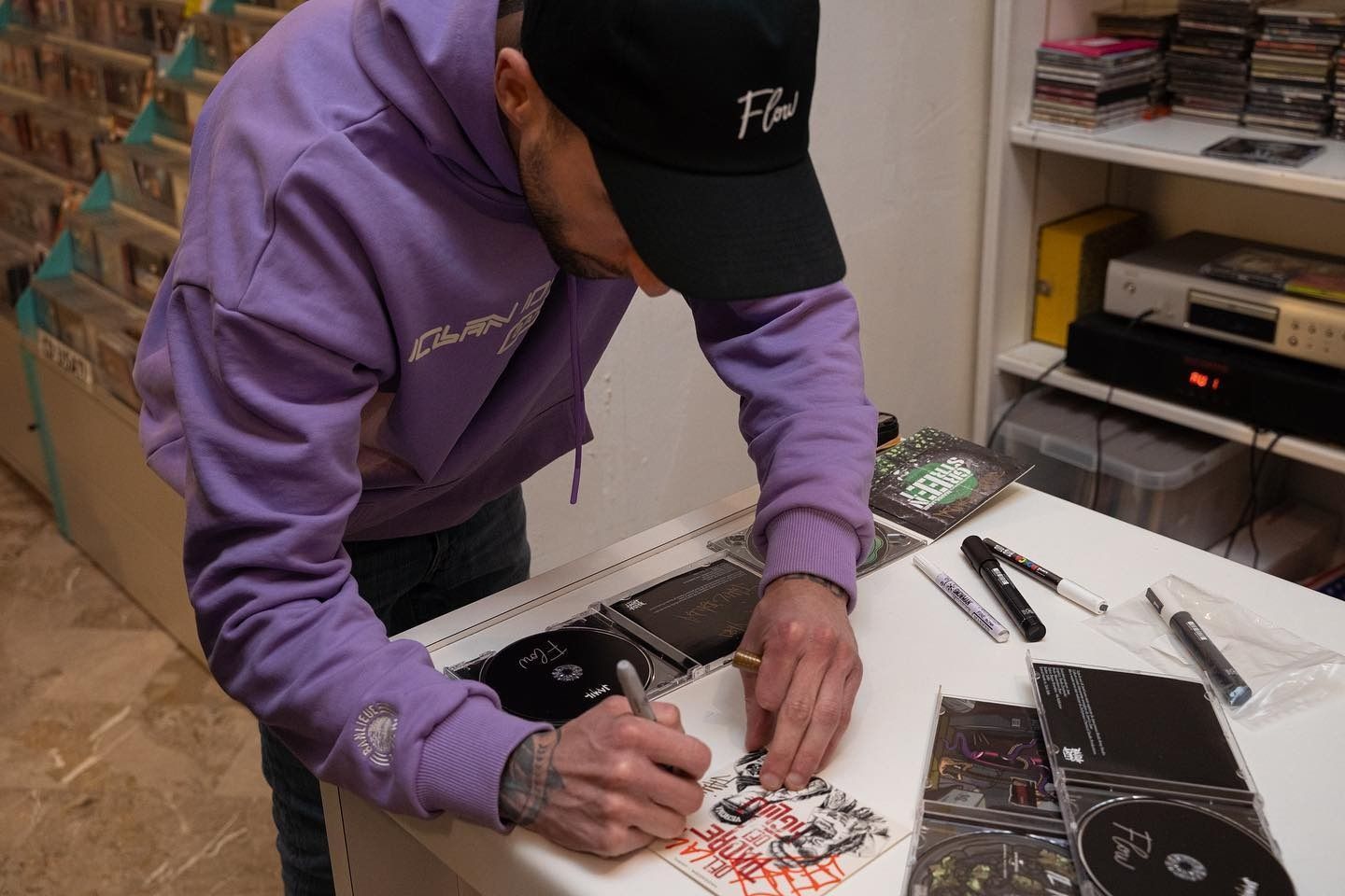 Un uomo con una felpa viola e un cappello nero sta firmando un cd.