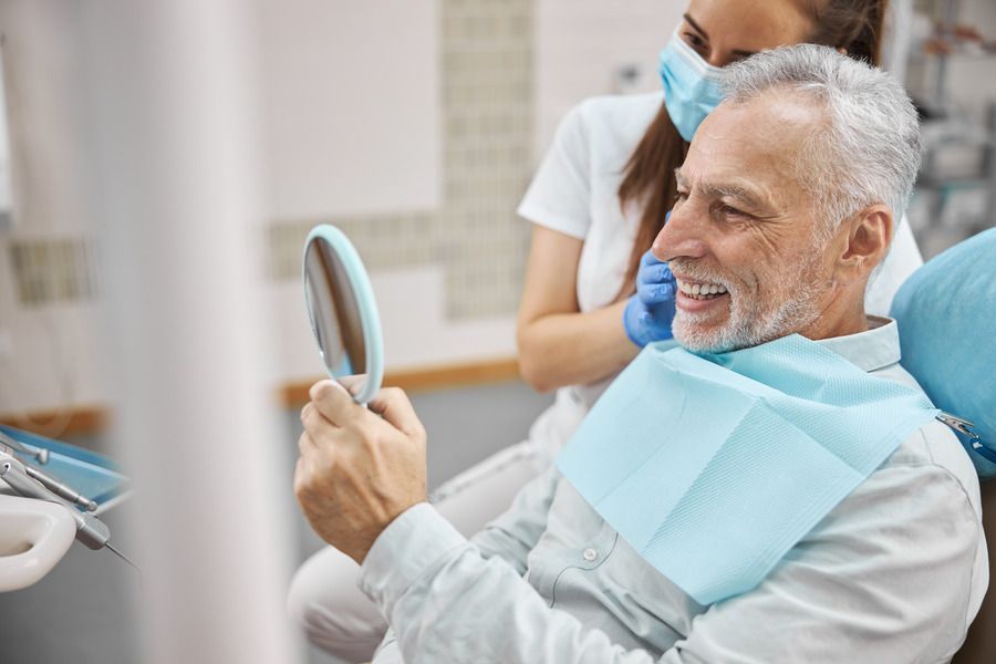 man looking into mirror smiling at dentist | dental implants Monroe township and Highland Park NJ