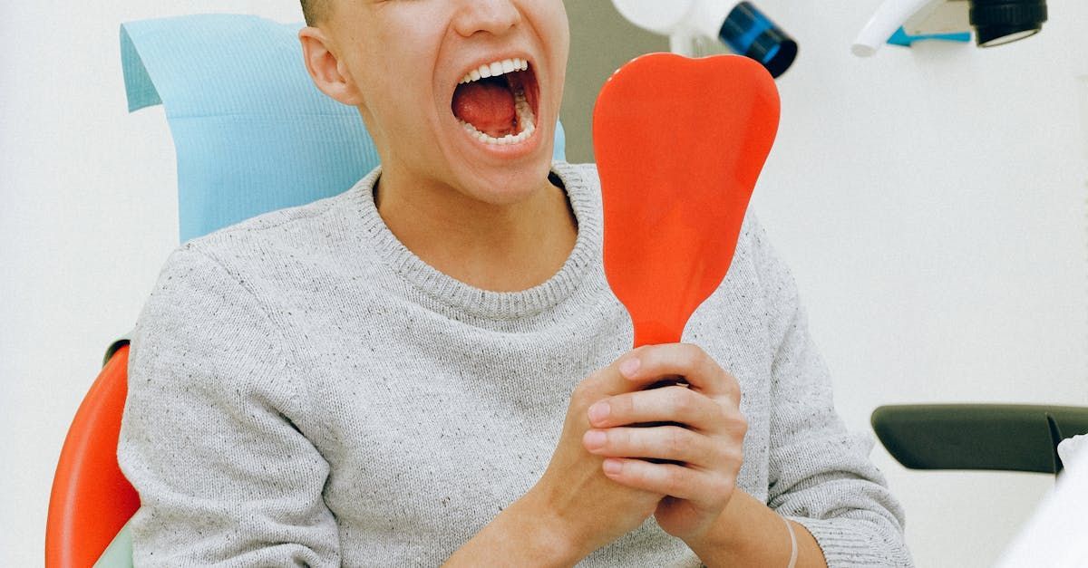 A woman is sitting in a dental chair looking at her teeth in a mirror.