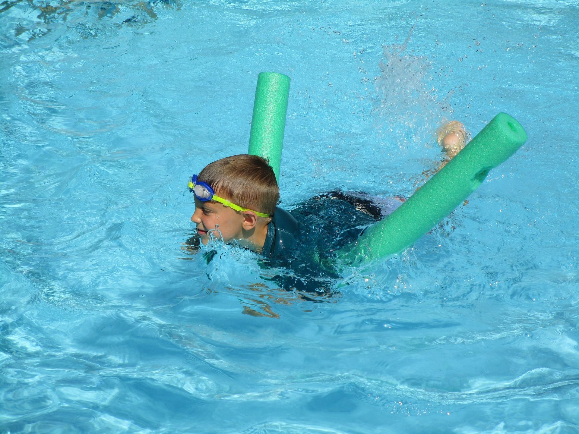 A young boy is swimming in a pool with a green noodle.