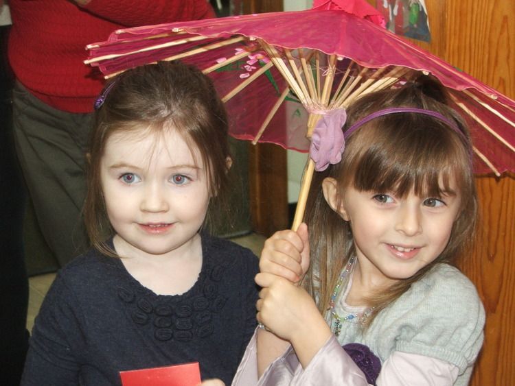 Two little girls are holding pink umbrellas and smiling for the camera