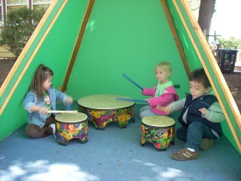 Three children are playing drums in a green teepee
