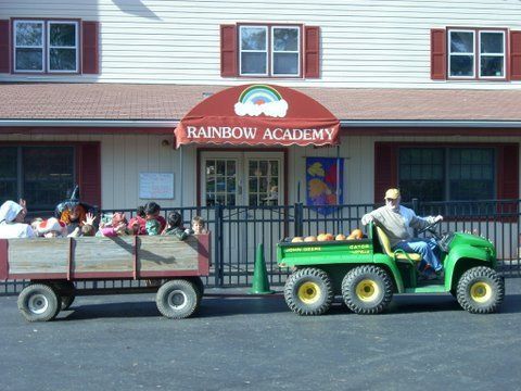 A tractor pulling a trailer full of children is parked in front of the rainbow academy