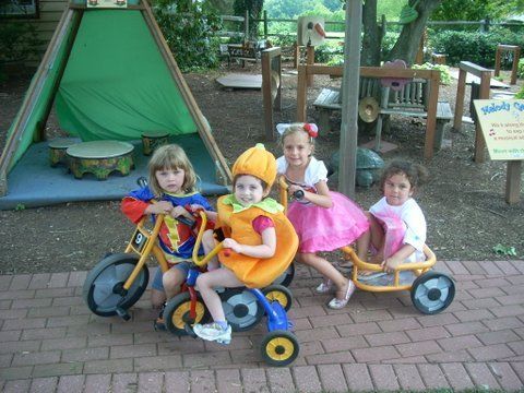 Three little girls are riding tricycles on a brick sidewalk