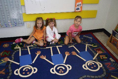 Three little girls are sitting on a rug in a classroom