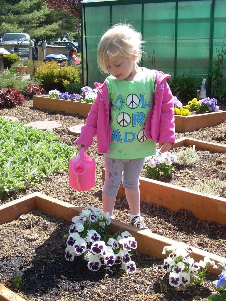 A little girl wearing a green shirt that says cool or rad is watering flowers