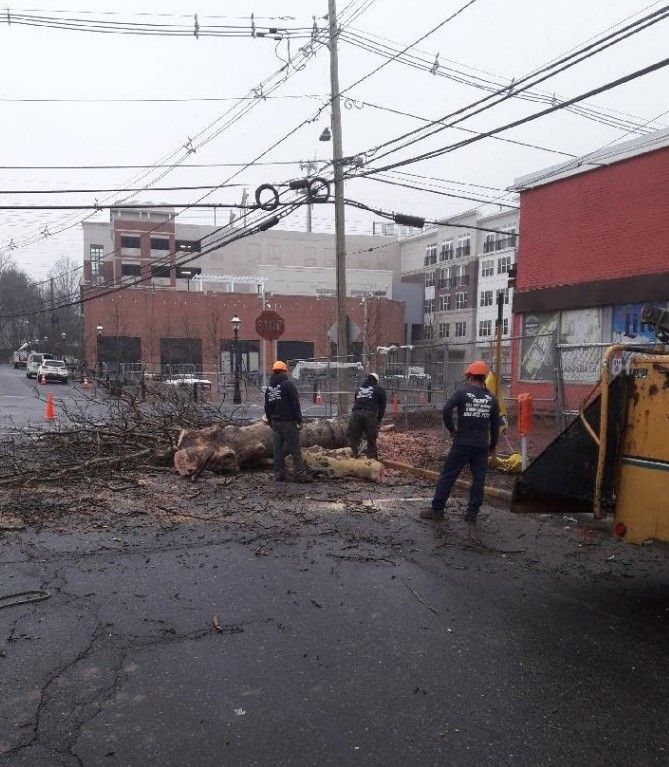 Workers clearing debris from a wet street near downed utility lines after a storm