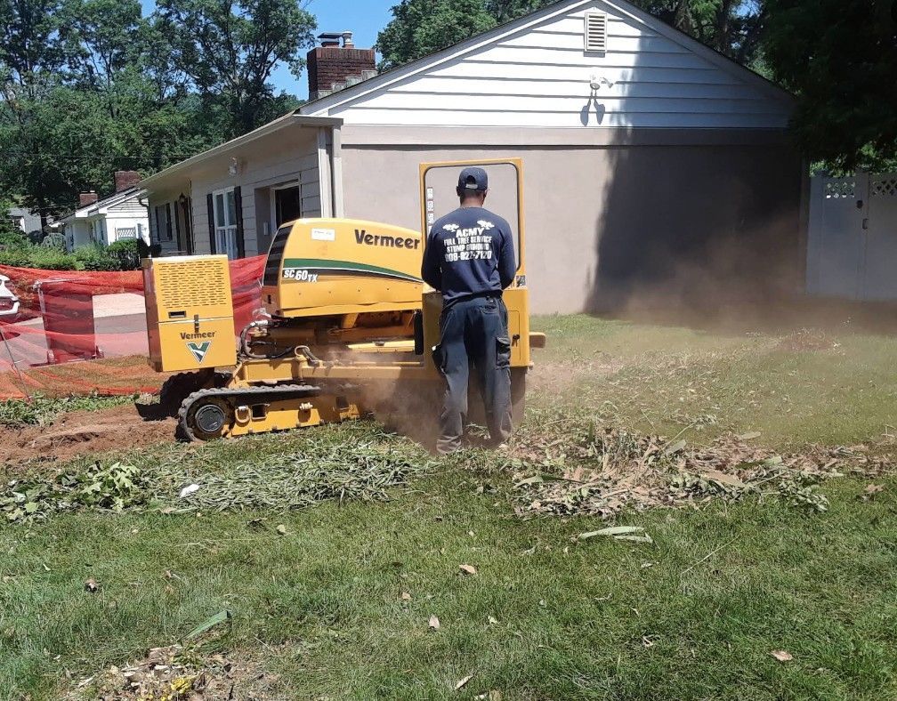 Worker using a yellow wood chipper to clear brush beside a house, with dust blowing out the side.