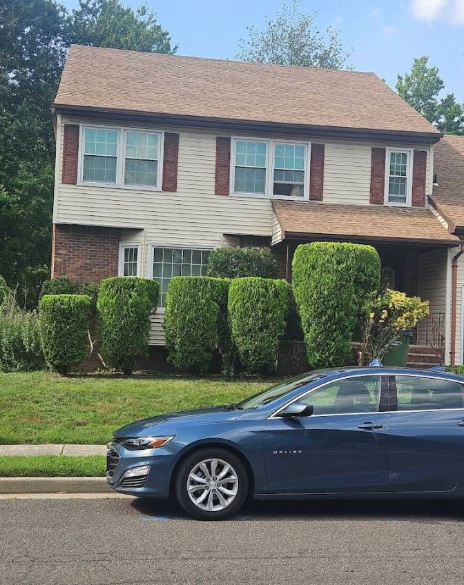 Two-story suburban house with trimmed hedges and a blue sedan parked in front.