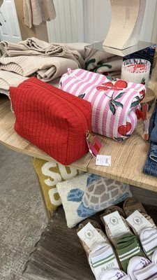 Two makeup pouches—one solid red, one pink and white striped with cherry prints—sit on a wooden store display shelf.