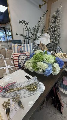 A retail display featuring a floral arrangement, striped pillows with an oyster motif, serving trays, and a small tree.