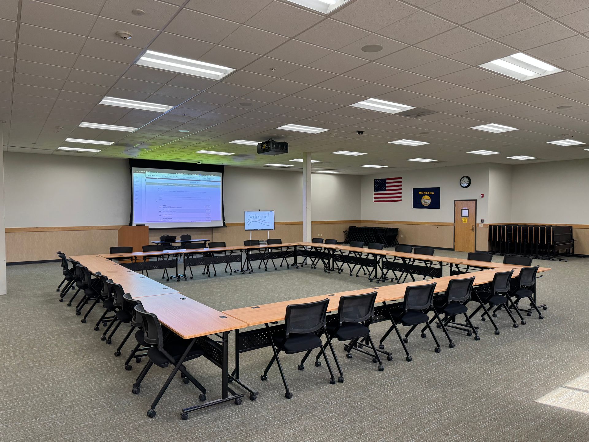 A large room with tables and chairs and a projector screen.