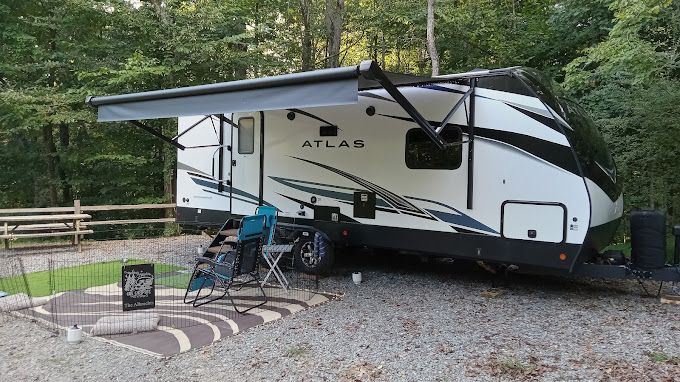 A white and black rv with an awning is parked in a gravel lot.