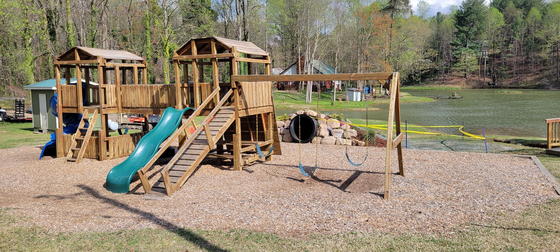 A wooden playground with a slide and swings next to a lake.