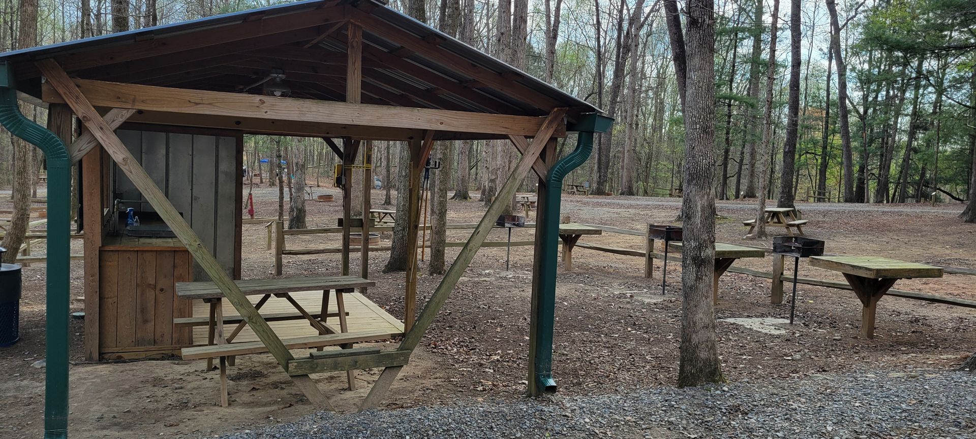 A wooden shelter with a picnic table underneath it in the tent area