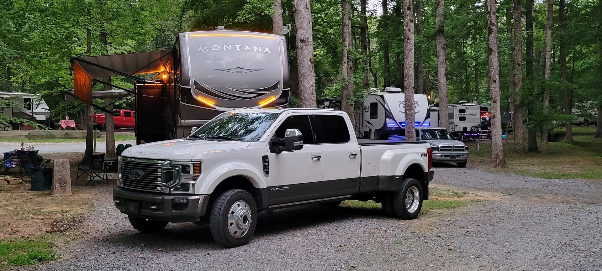 A white truck is parked in a gravel lot next to a rv.