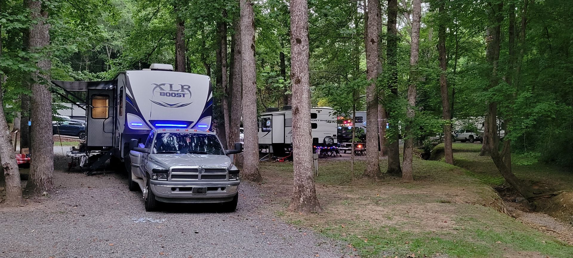 A truck is parked next to a rv in the woods.