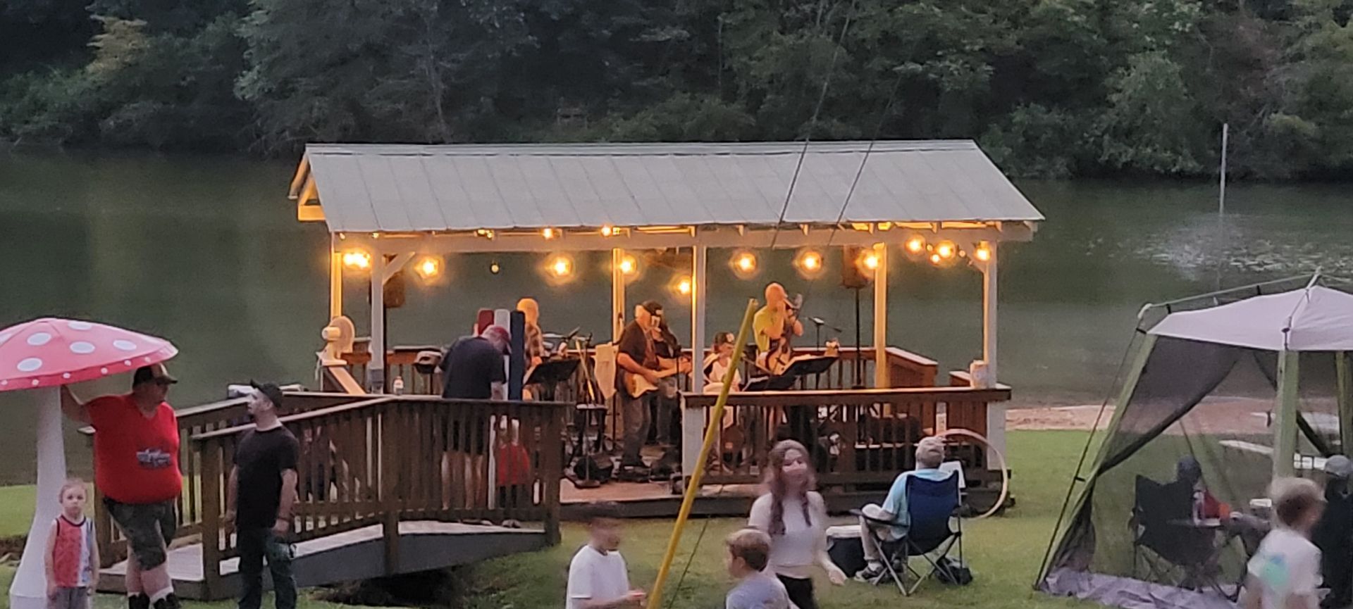 A group of people are gathered under a gazebo near a lake.