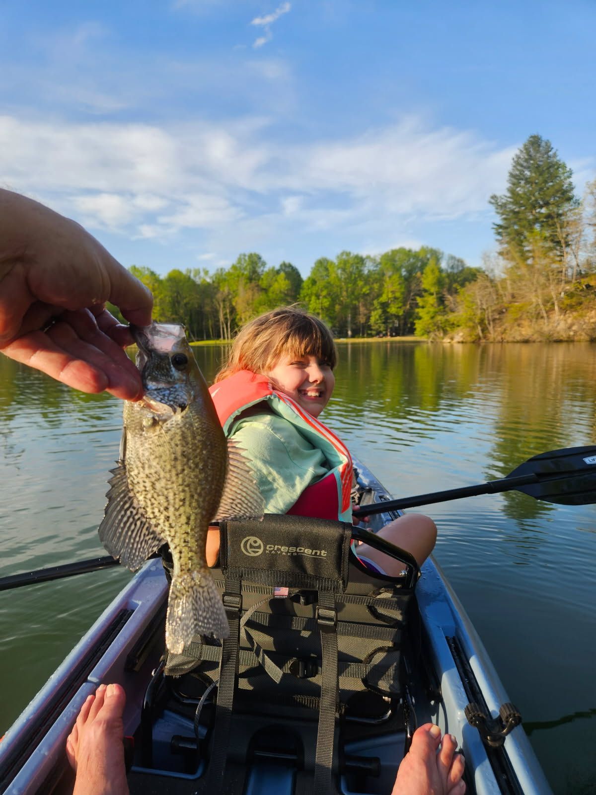 A person is holding a fish in front of a child in a kayak