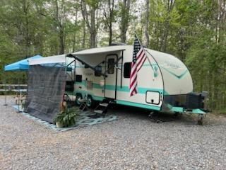 A white and green rv is parked in a gravel lot in the woods.