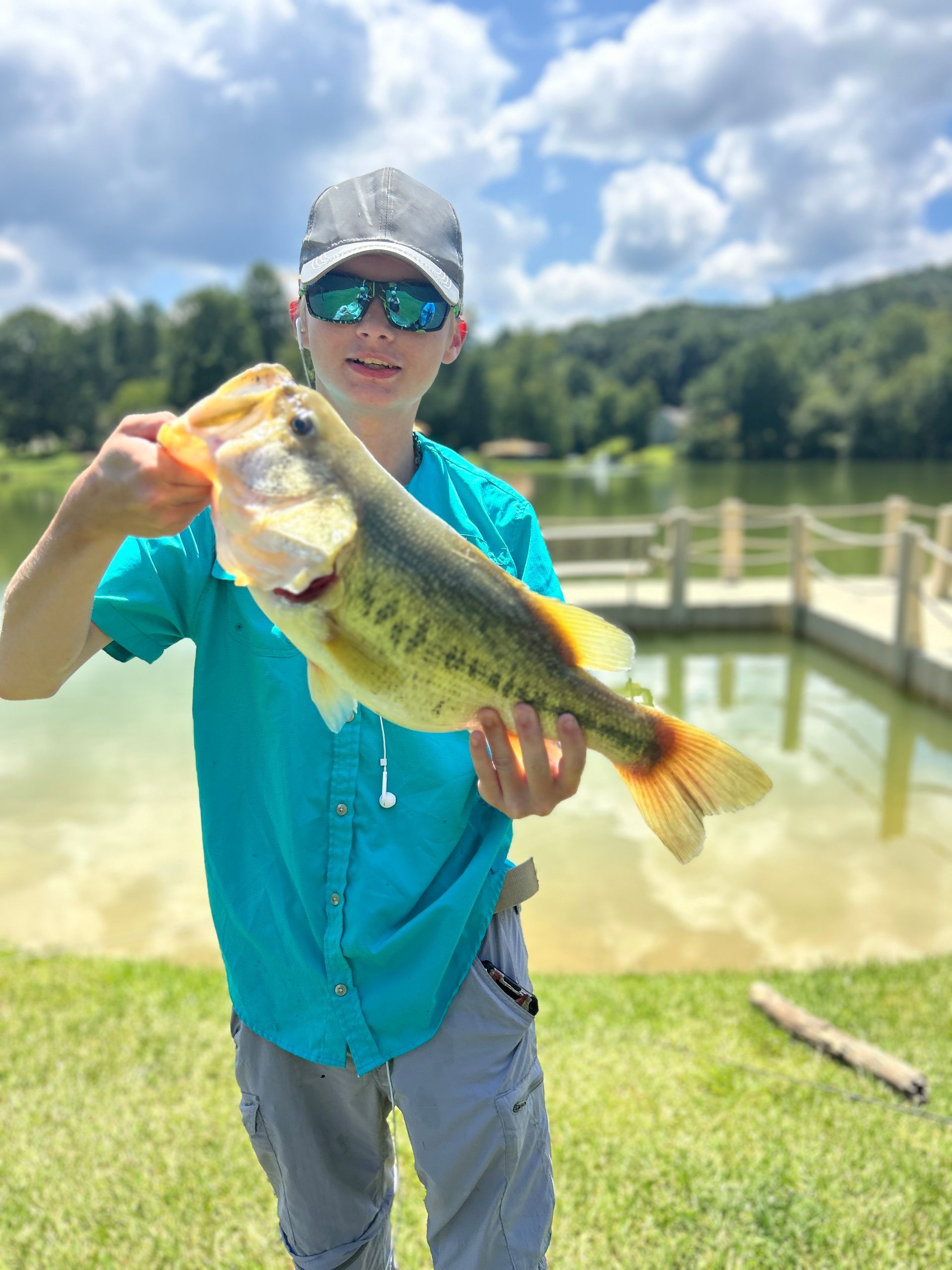 A boy is holding a large fish in front of a lake