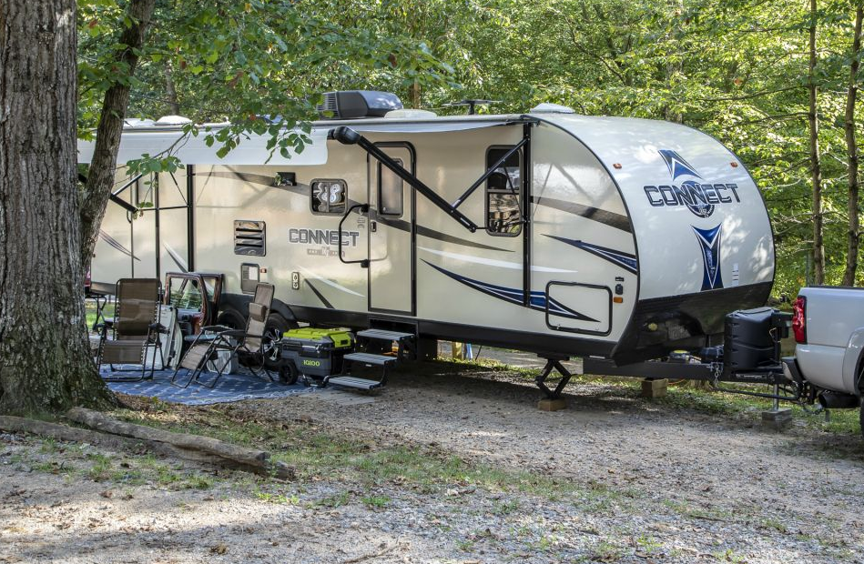 A white rv is parked in a gravel lot in the woods.