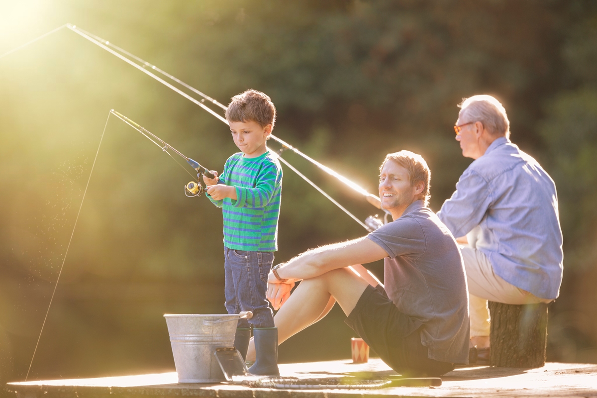 A little boy is fishing with his father and grandfather