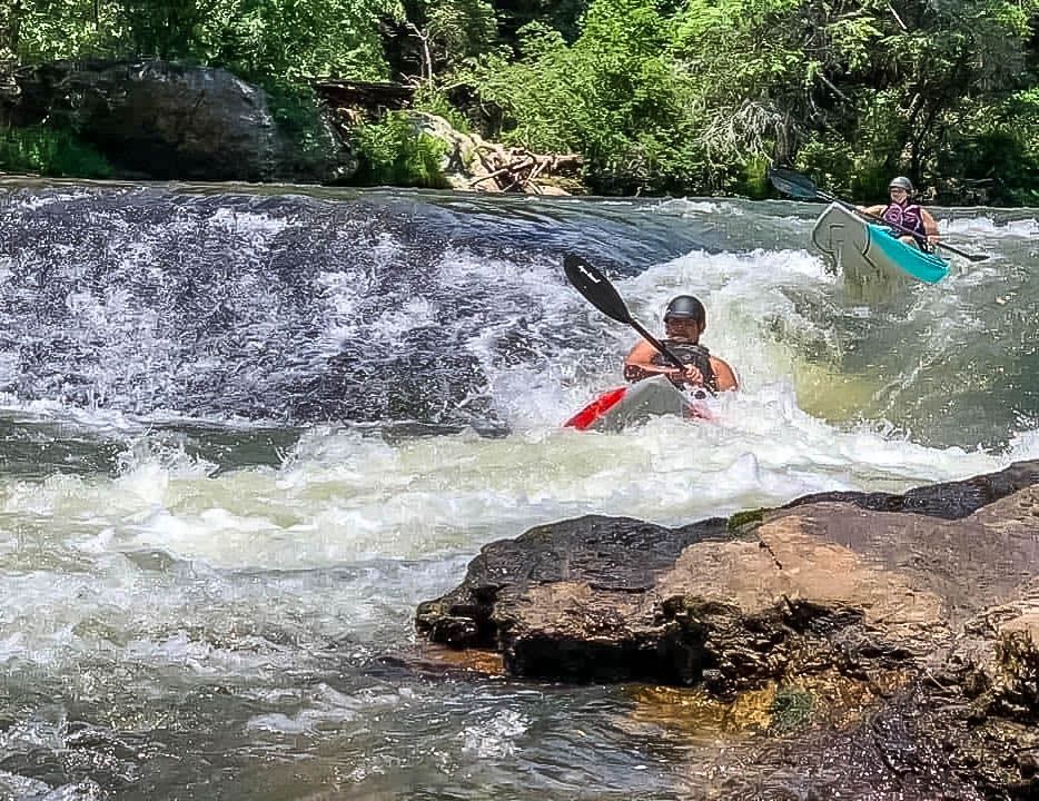 A man is riding a wave in a kayak on a river.