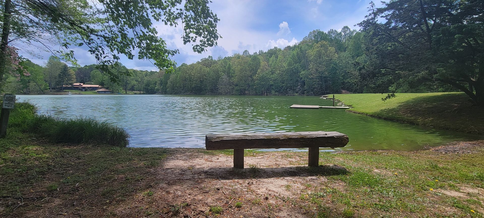 A wooden bench sits in front of a lake surrounded by trees
