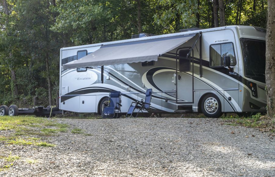 A rv with an awning is parked in a gravel lot