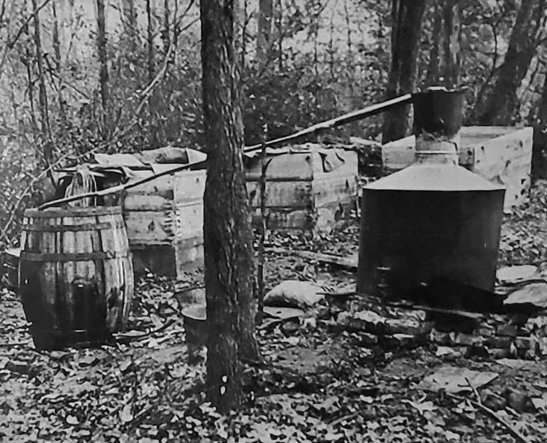 A black and white photo of a distillery in the woods