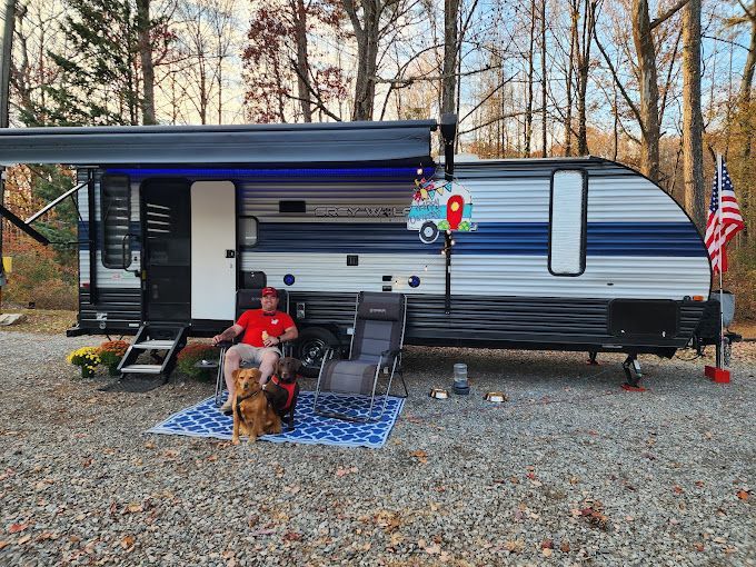 A man is sitting in front of a trailer with a dog.