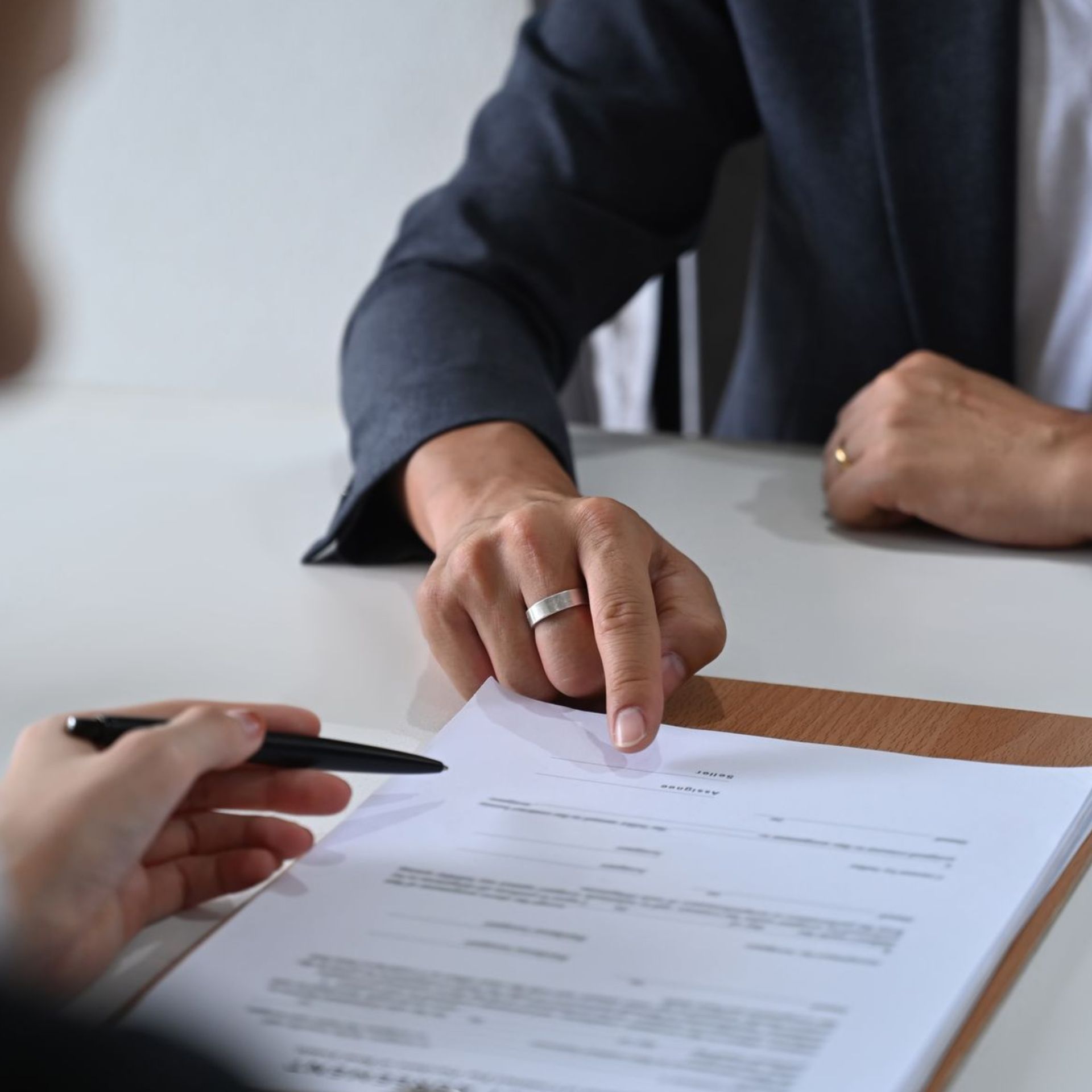 Two people reviewing and signing a document at a desk with a pen and clipboard.