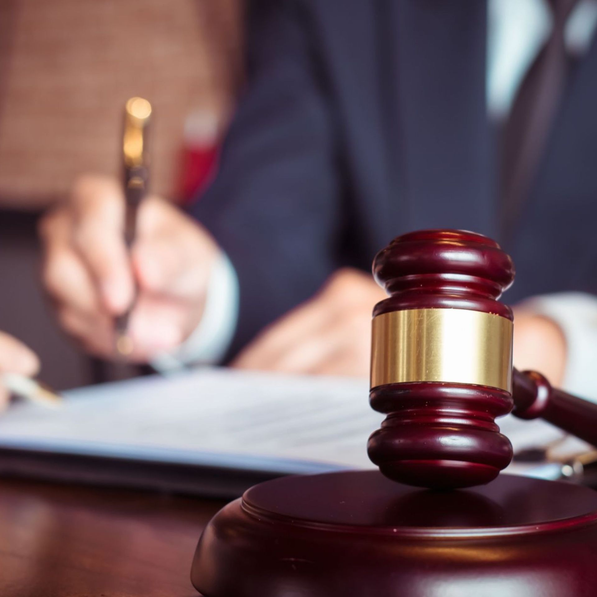 Judge's gavel on a desk with blurred lawyers writing in the background