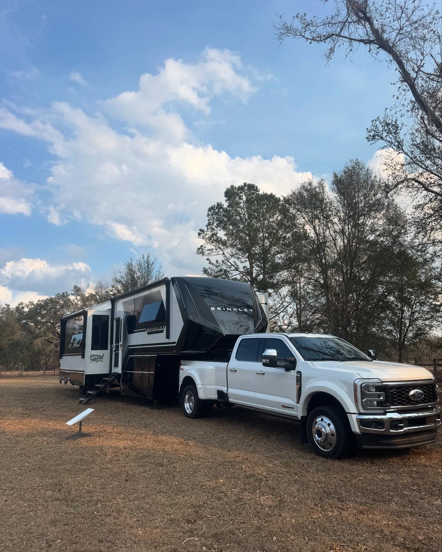 A white truck is towing a trailer in a gravel lot.