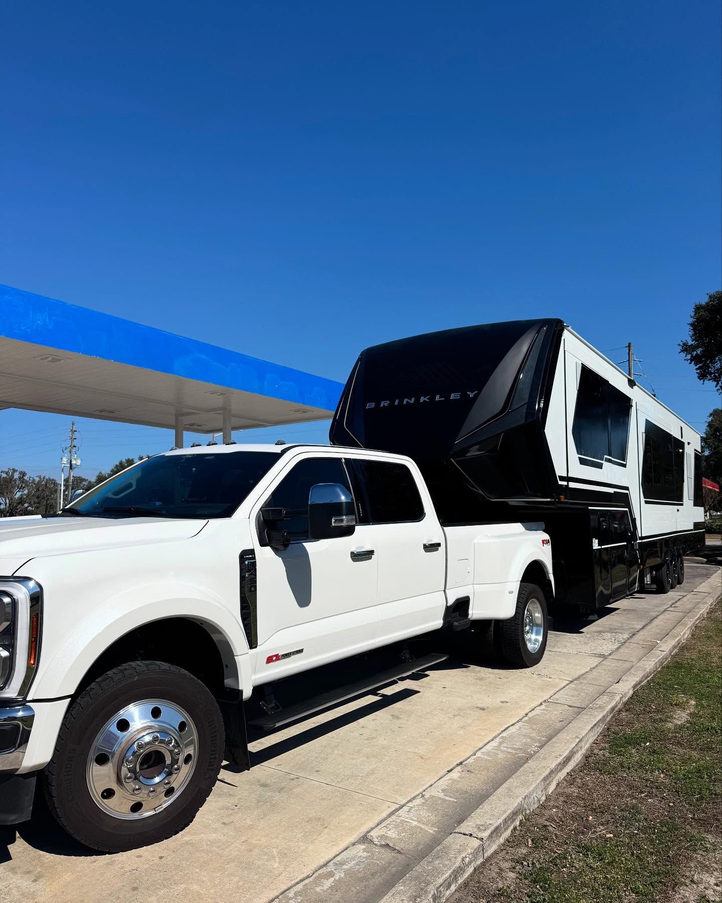 A white truck is towing a black trailer at a gas station.