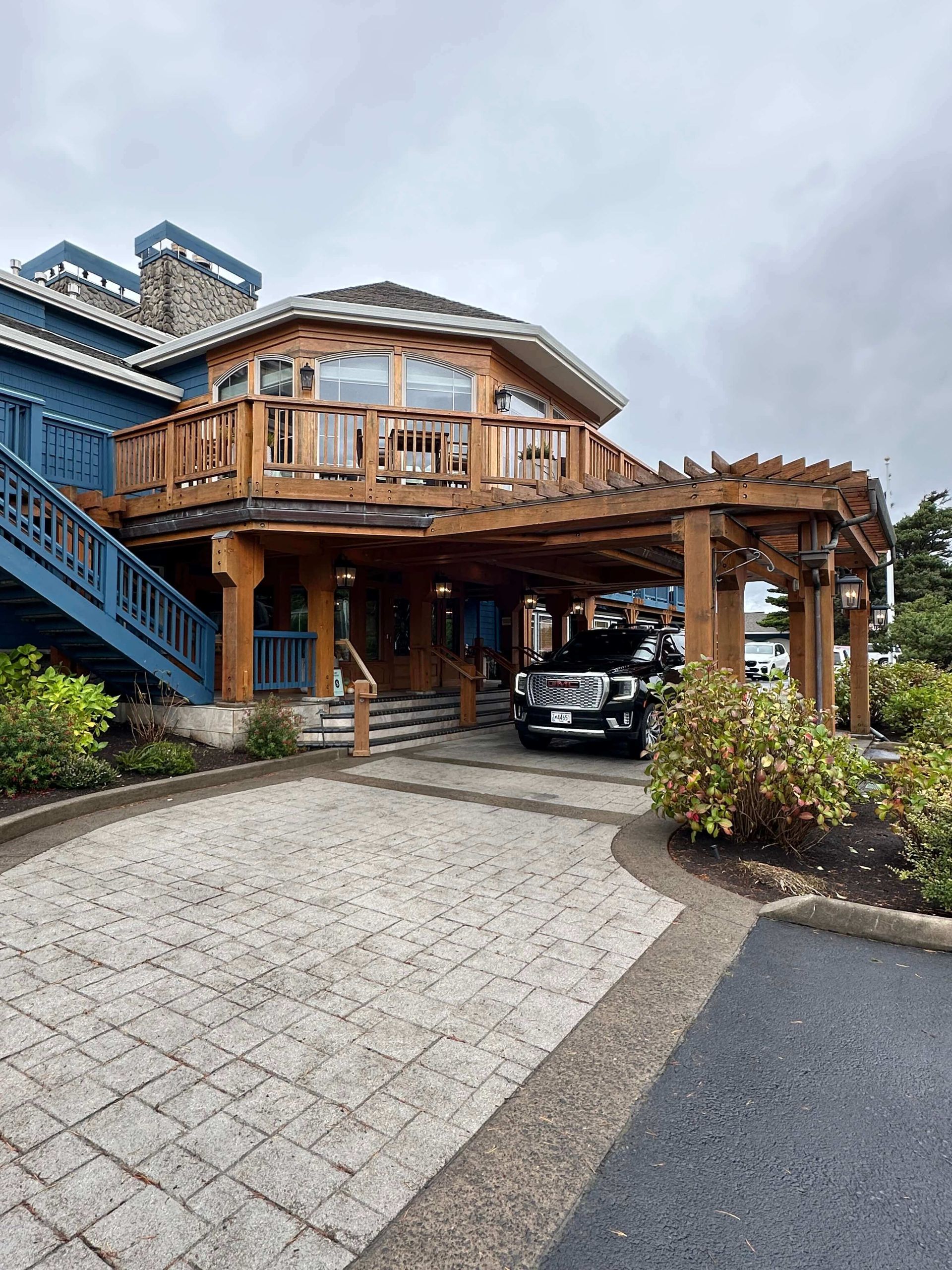 Blue building with wooden accents; black limousine parked under a wooden pergola. Brick driveway, Cannon Beach Oregon