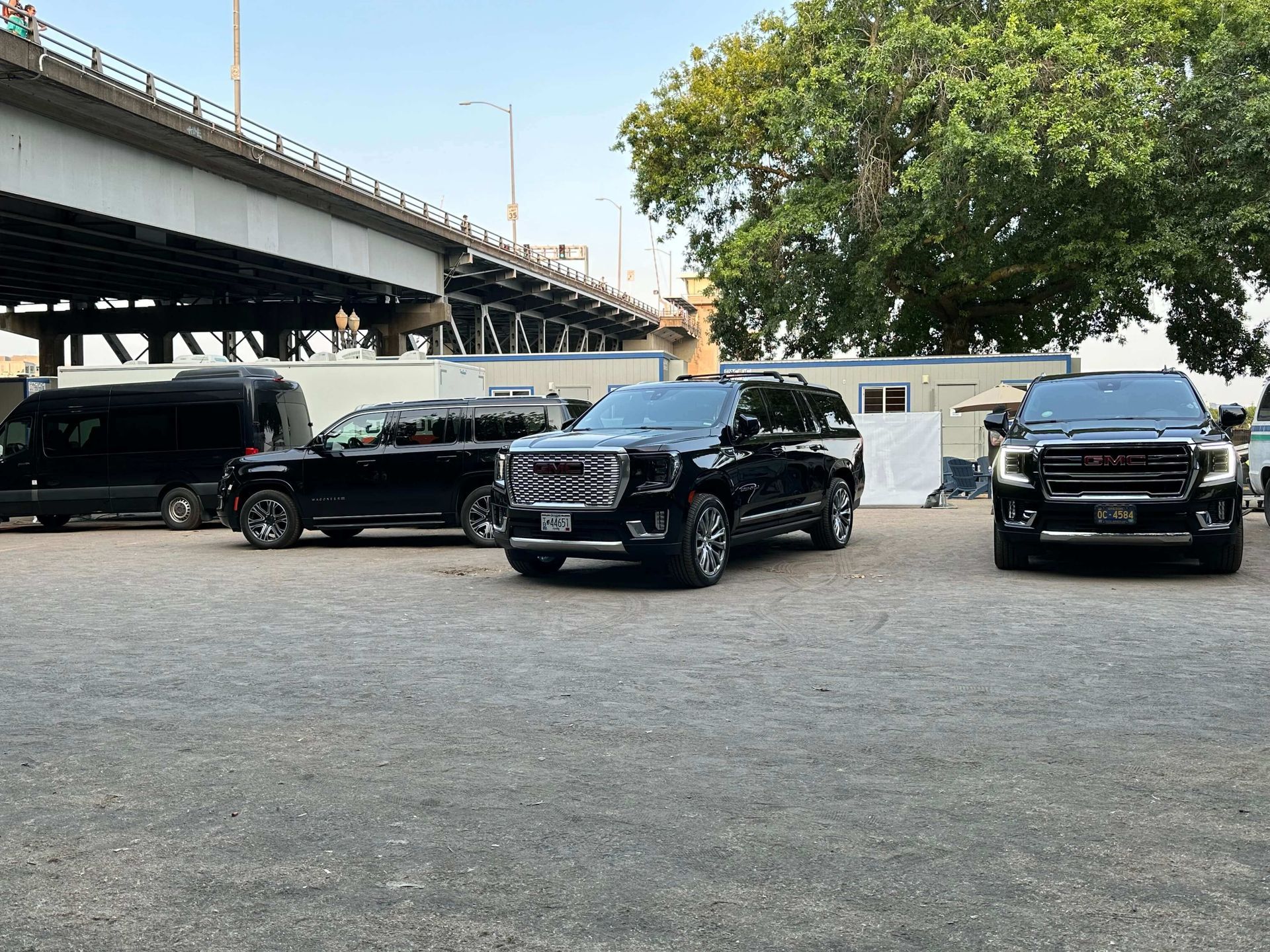 Black SUVs parked on gravel near a bridge and trees in Portland Oregon