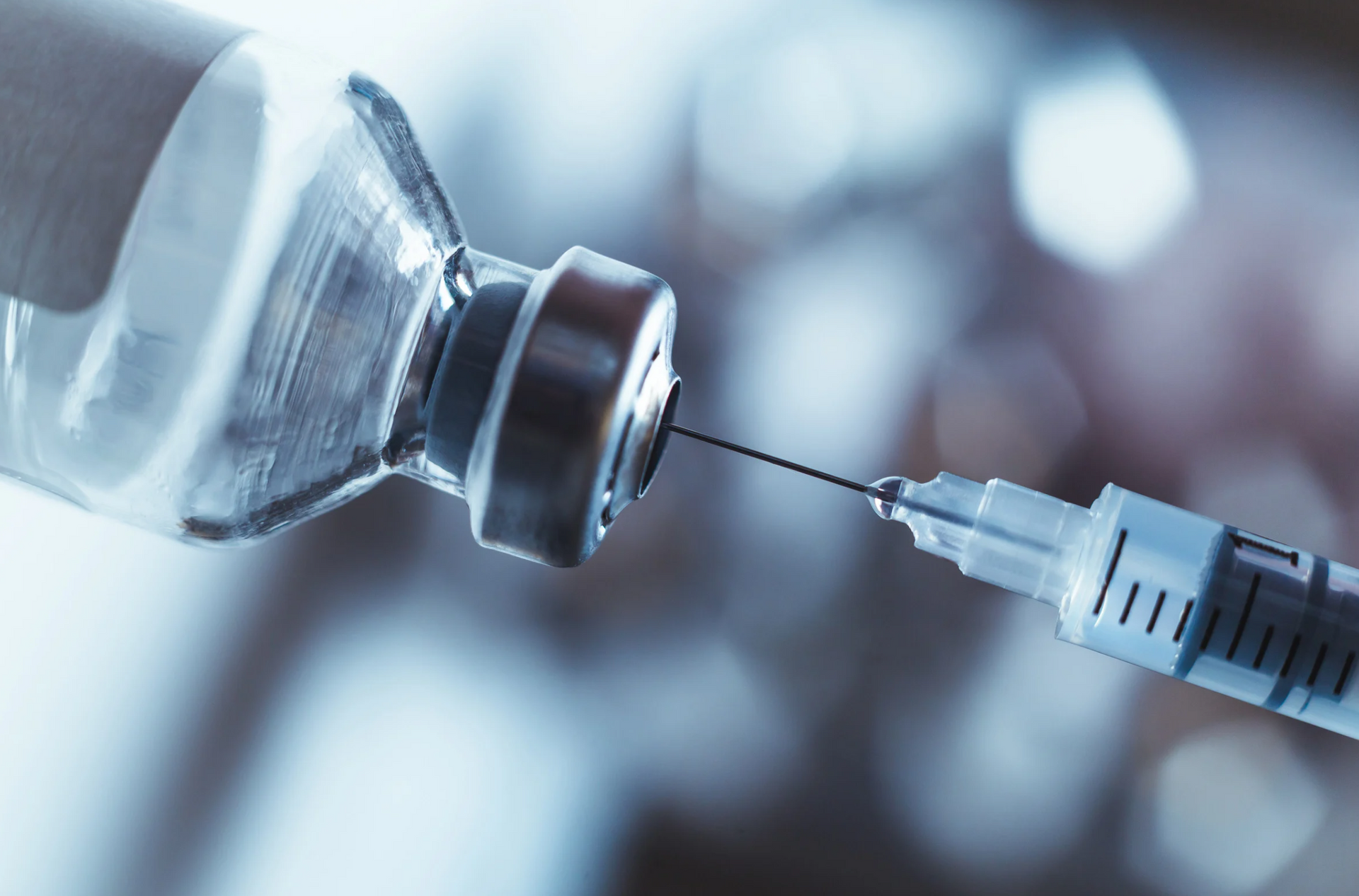 Syringe needle injecting a vial with a blue-tinted background.