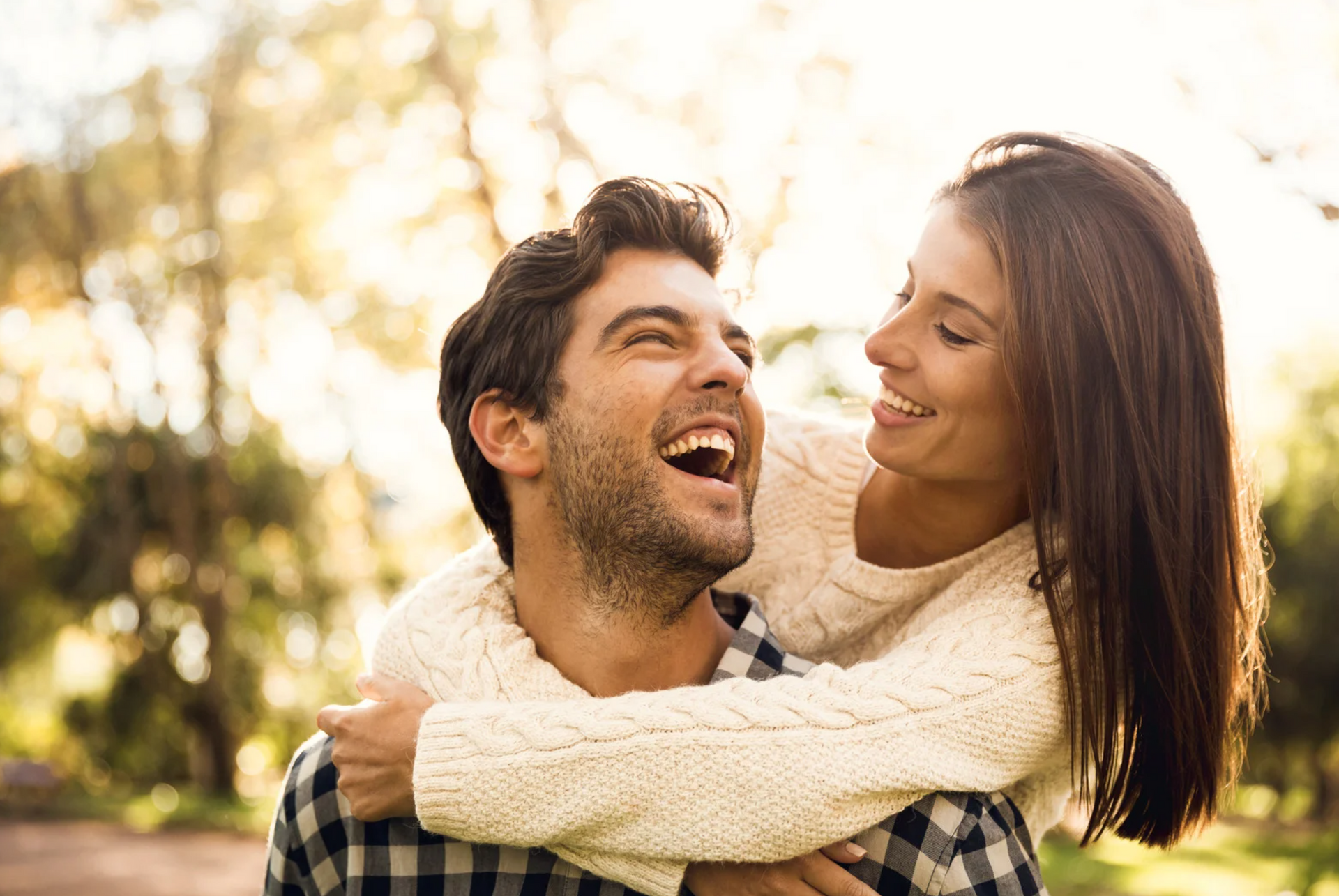 Woman hugging a laughing man, smiling in a park, both enjoying a sunny day.