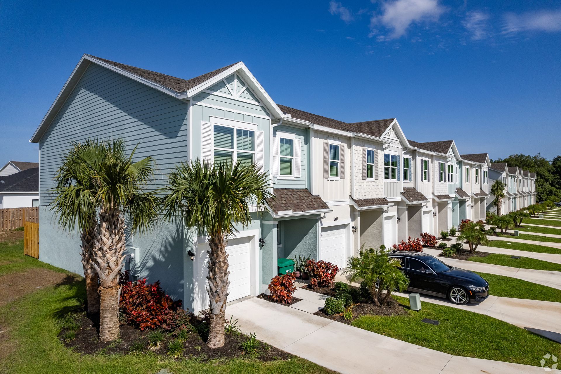 Row of blue and white townhouses with palm trees and cars parked in the driveways.