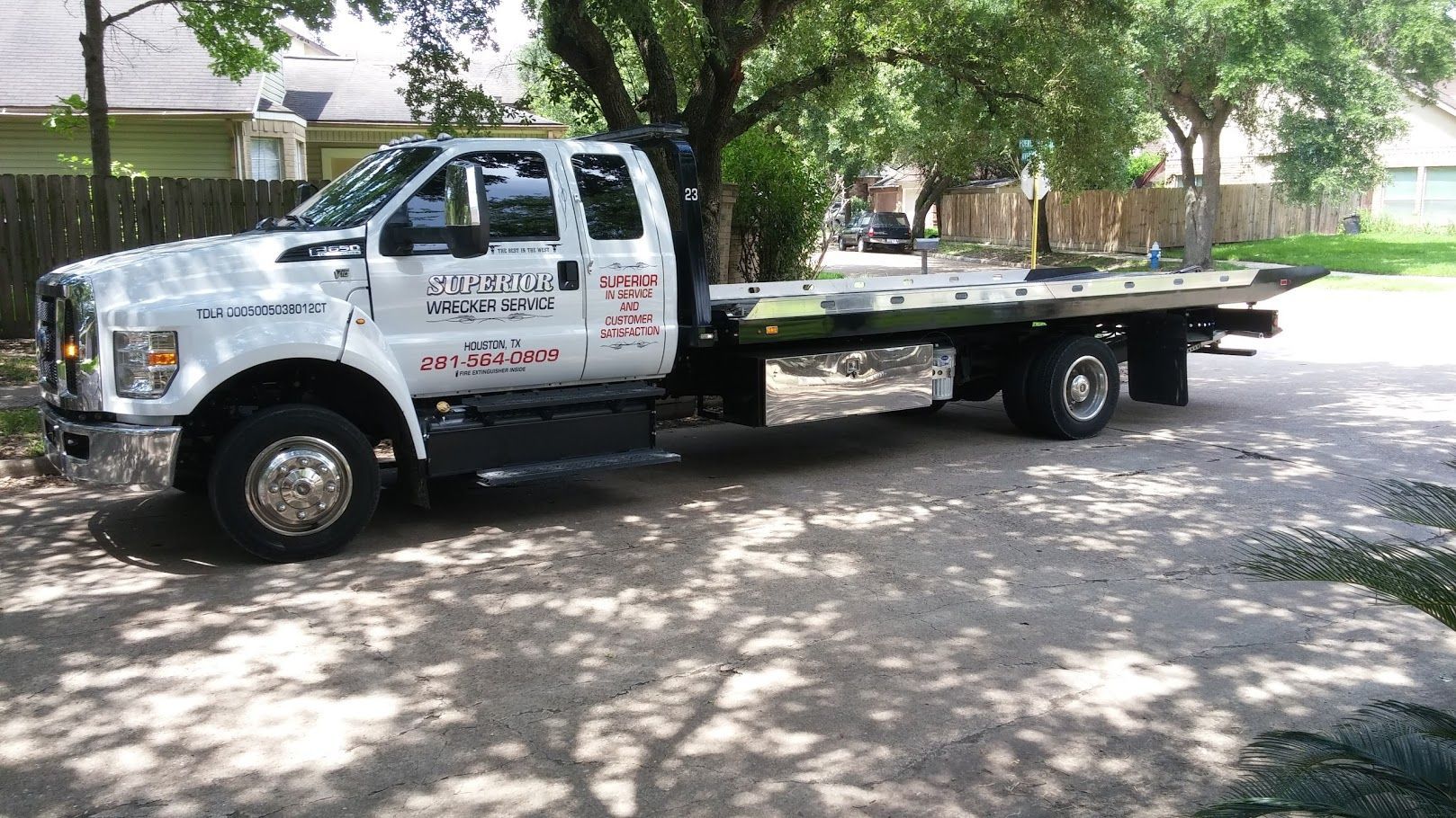 White tow truck parked on a driveway with trees and houses in the background
