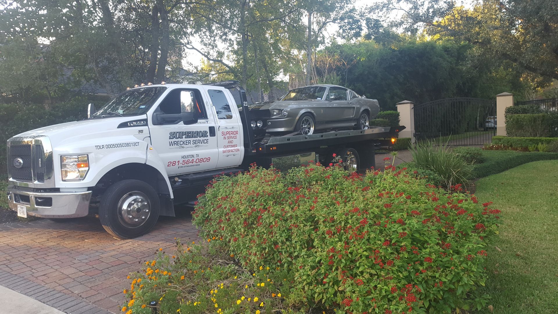 Tow truck carrying a gray classic car on a residential driveway