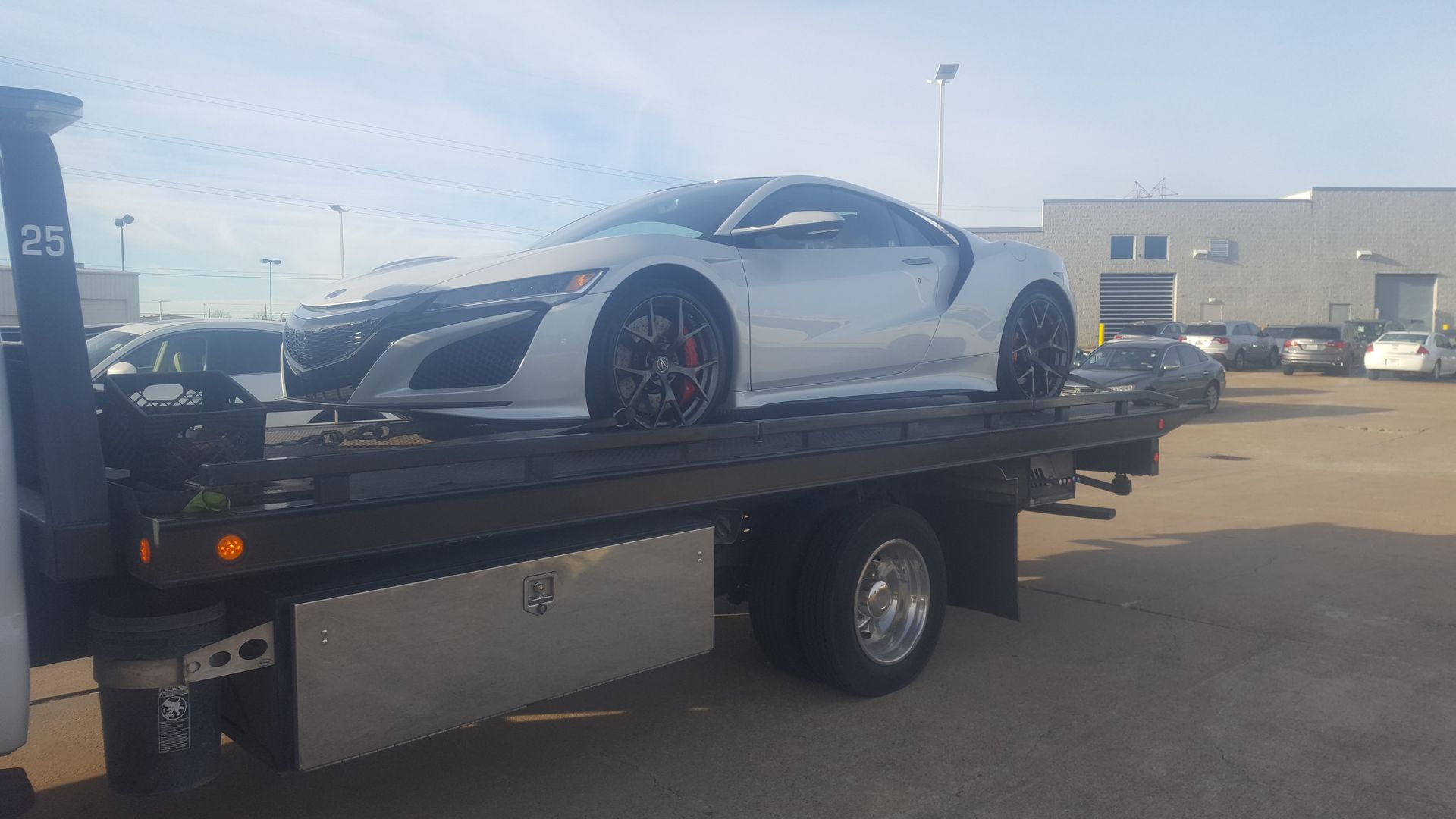 Silver sports car on a flatbed tow truck outdoors on a sunny day