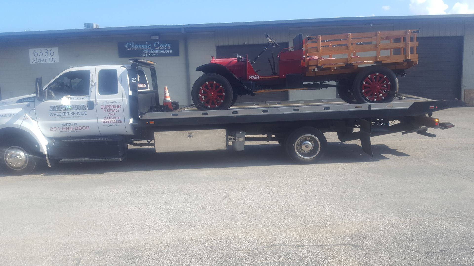 Red vintage truck on a flatbed tow truck in front of a building with a blue sky