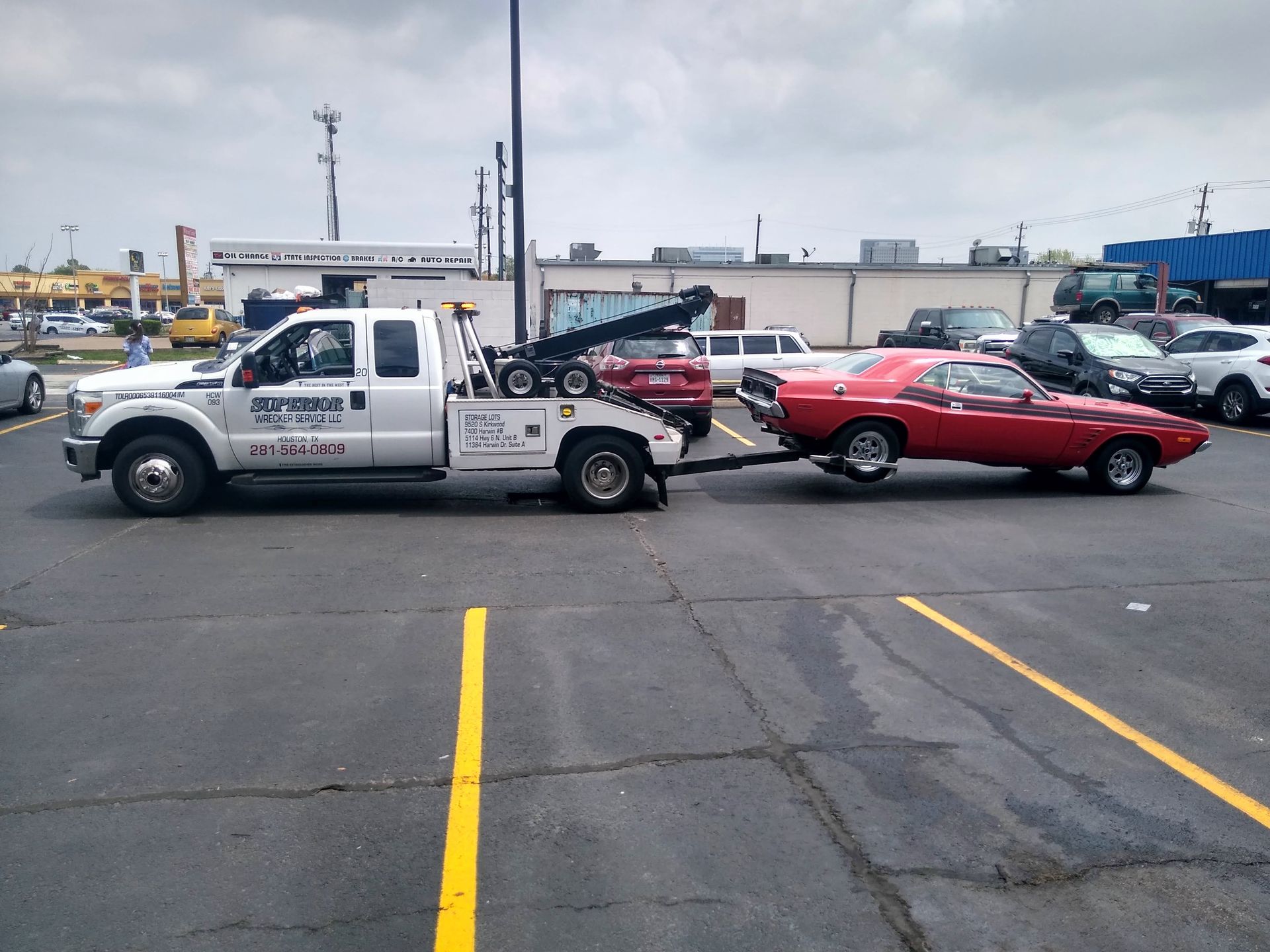 A white tow truck towing a red classic car in a parking lot on a cloudy day