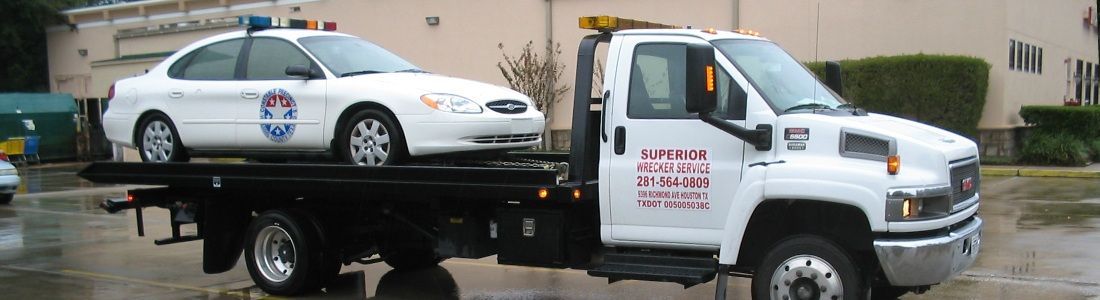 A white police car is being towed on a flatbed truck on a rainy day